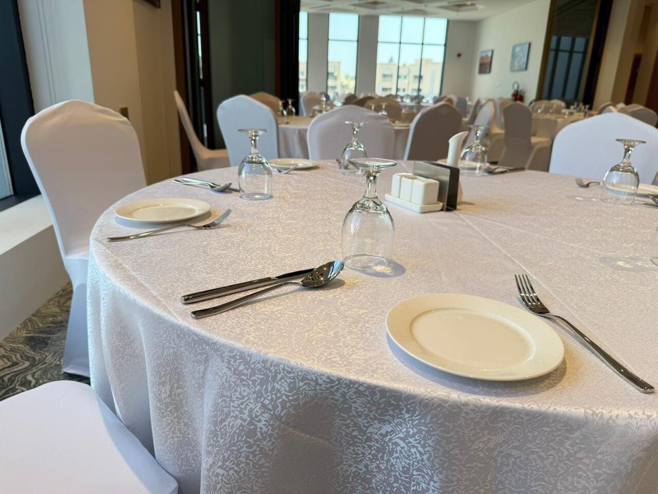 A round table set for dining with white tablecloth, chairs, and glassware.