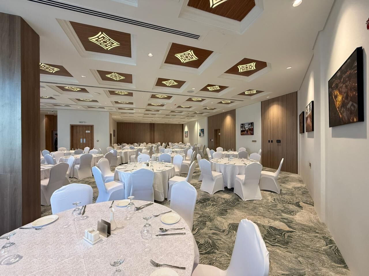 Un salón de conferencias con mesas redondas, sillas blancas y una alfombra estampada.