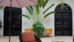 Een kamer met een grote potplant, twee rieten stoelen, een klein tafeltje en een zwarte deur.
