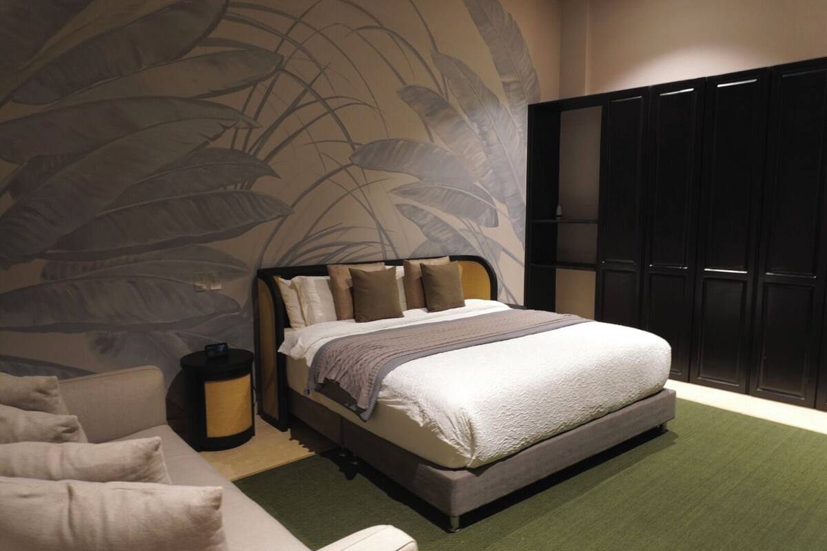 Un dormitorio con cama, mesita de noche, silla, armario y pared con diseño de hojas.
