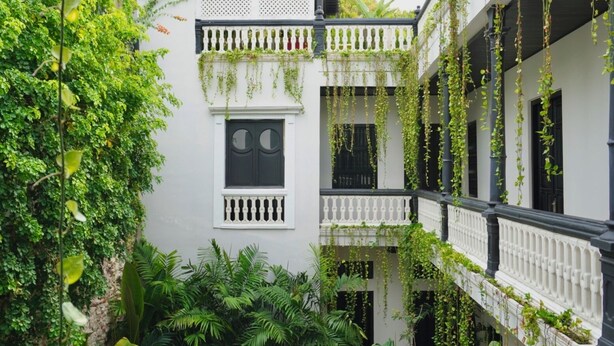 Een wit gebouw met meerdere balkons, waarvan sommige begroeid zijn, en een centraal raam met een witte balustrade.