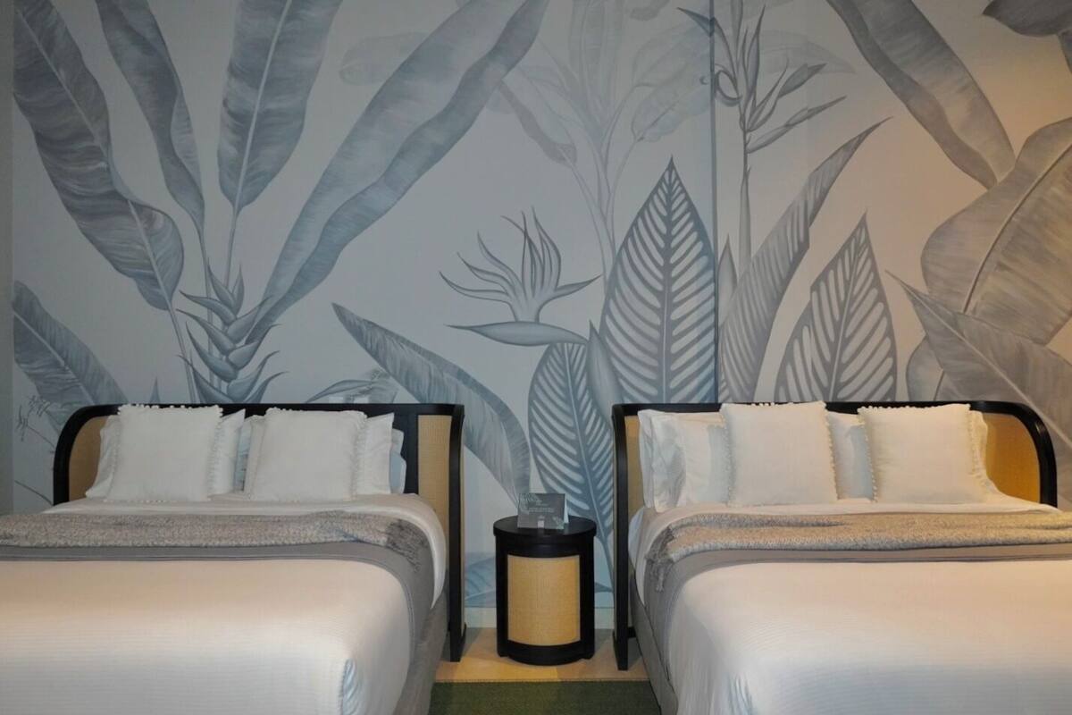 Una habitación con dos camas, una mesita de noche y una pared con estampado de hojas.