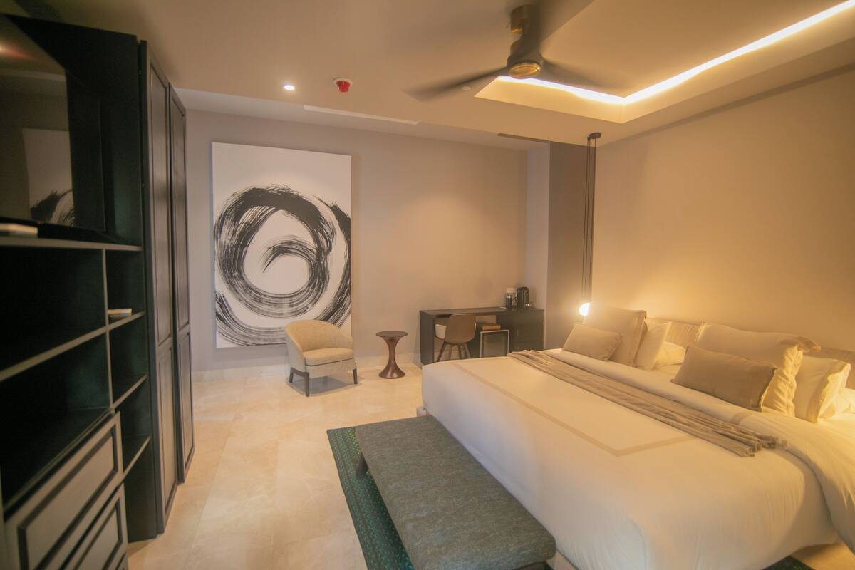 Una habitación de hotel moderna con una cama grande, un escritorio, una silla y un armario.