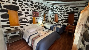 Habitación con paredes de piedra, dos camas, suelo de madera y una pequeña mesa.
