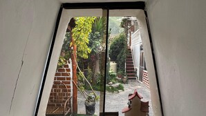 Una habitación con techo inclinado, una ventana con vista a un jardín y una pequeña mesa.