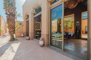 A restaurant with outdoor seating, palm trees, and large vases.