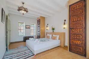 Un dormitorio espacioso con una cama grande, una puerta de madera y una lámpara decorativa en el techo.
