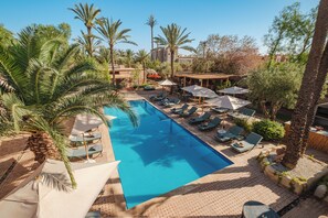 A swimming pool with lounge chairs and umbrellas, surrounded by palm trees and a building in the background. - Hotel Dar 55 Berbere House & Spa (Marrakech)