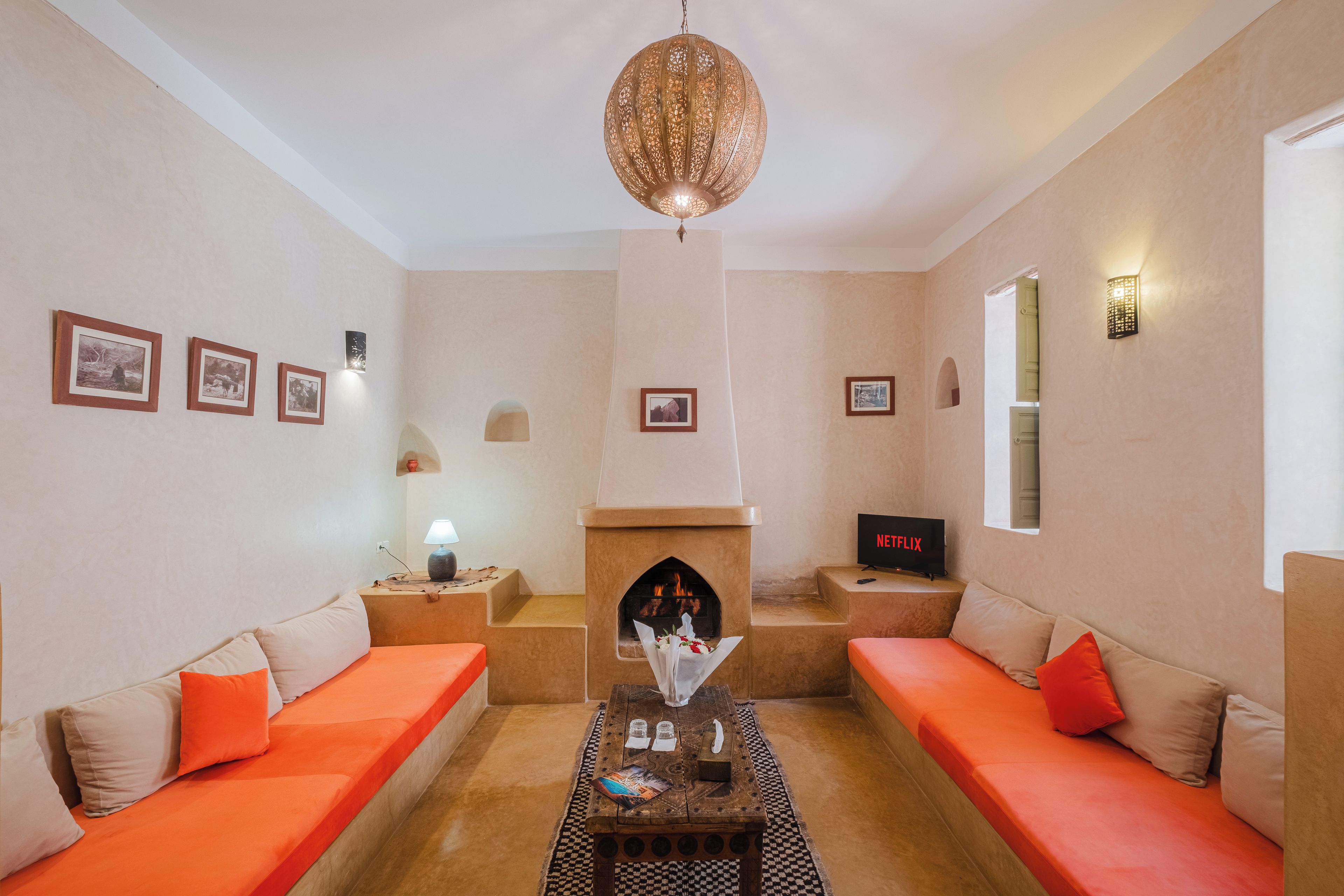 A living room with two orange sofas, a fireplace, a television, and framed pictures on the wall.