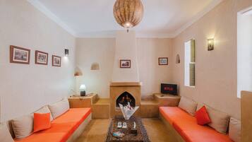 A living room with two orange sofas, a fireplace, a television, and framed pictures on the wall.