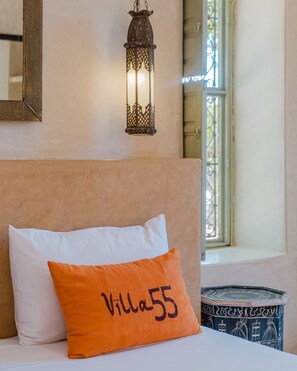 A bed with a white pillow and an orange pillow with 'Villa 55' text, a hanging lantern, and a window with a view. - Hotel Dar 55 Berbere House & Spa (Marrakech)