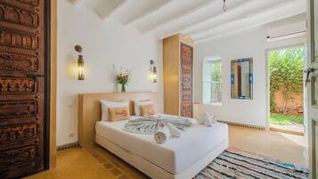 A bedroom with a large bed, a wooden door, a wall-mounted light, and a window.