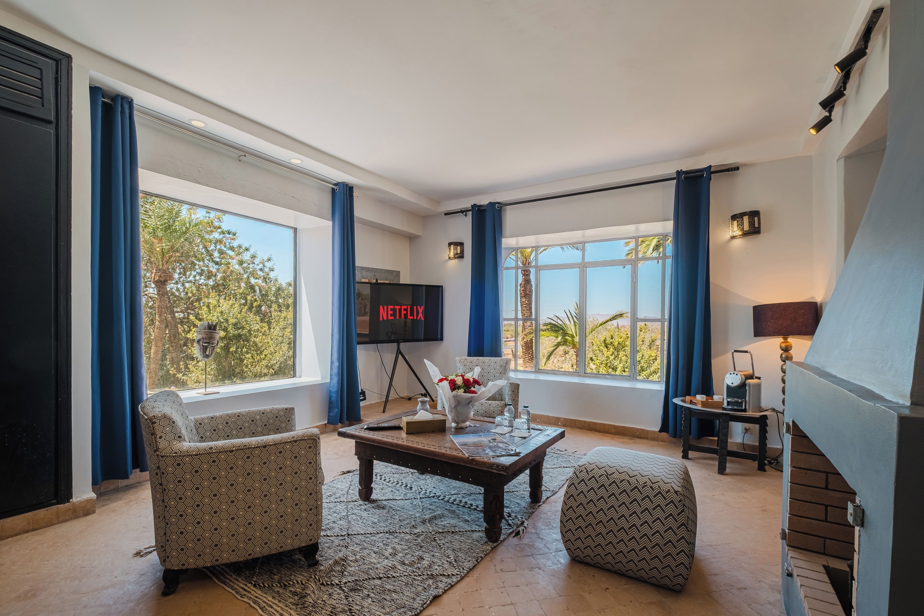 Una sala de estar con chimenea, televisor y un amplio ventanal con cortinas.