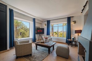 A living room with a fireplace, a television, and a large window with curtains. - Hotel Dar 55 Berbere House & Spa (Marrakech)