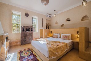 Un dormitorio con una cama grande, un aparador de madera, un tapete colorido y una ventana con celosía decorativa.