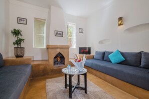 A living room with a fireplace, a sofa, a TV, and a potted plant. - Hotel Dar 55 Berbere House & Spa (Marrakech)