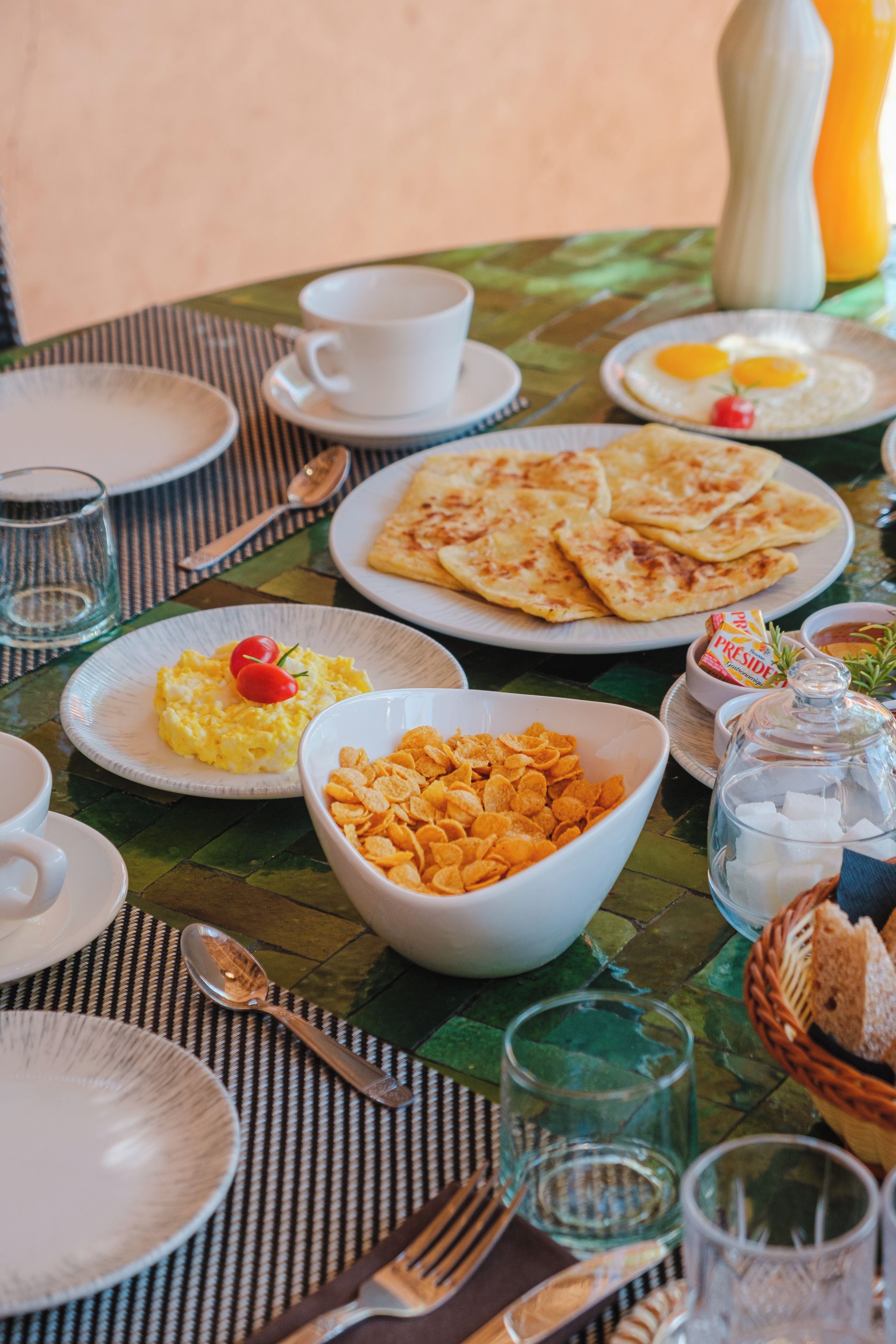 A breakfast setting with plates of eggs, toast, cereal, and a bowl of fruit.