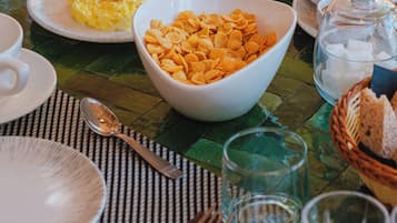 A breakfast setting with plates of eggs, toast, cereal, and a bowl of fruit.