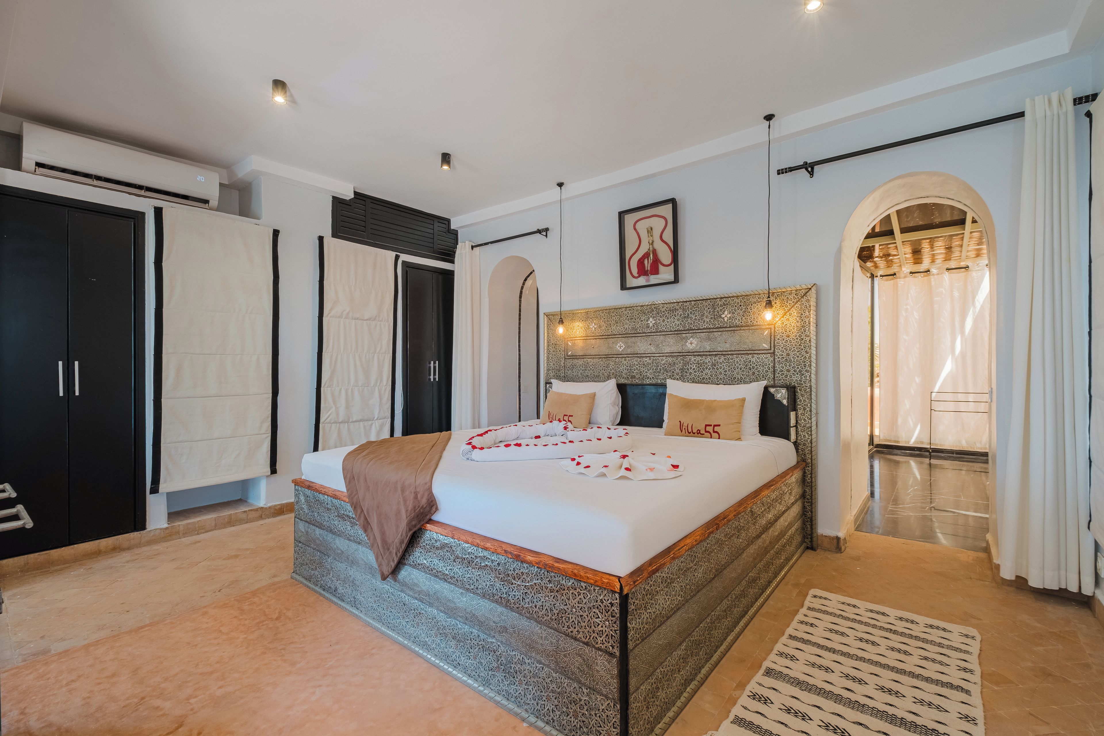 A spacious bedroom with a large bed, a wardrobe, and an arched doorway leading to a balcony.