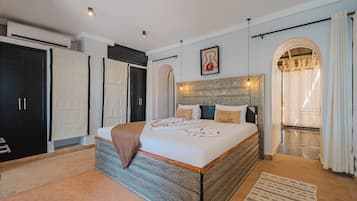 A spacious bedroom with a large bed, a wardrobe, and an arched doorway leading to a balcony.