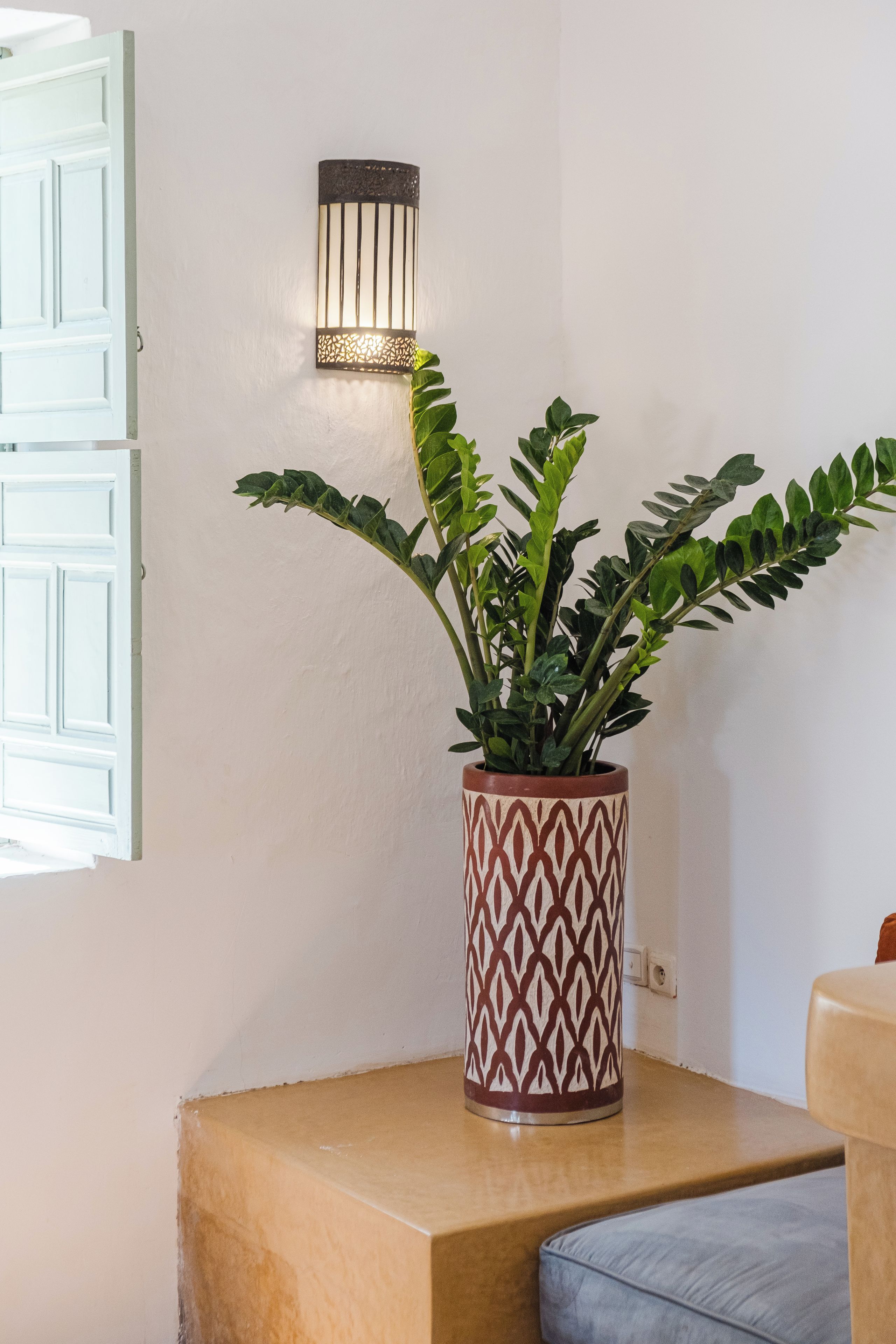 Ein Blumentopf auf einem Holztisch, eine an der Wand befestigte Leuchte und eine halb geöffnete weiße Tür.