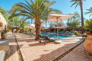A poolside area with lounge chairs, umbrellas, and a palm tree. - Hotel Dar 55 Berbere House & Spa (Marrakech)