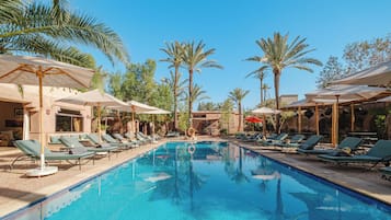 A swimming pool with lounge chairs and umbrellas, surrounded by palm trees.