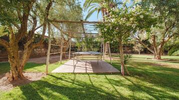 A wooden pergola with a table underneath, surrounded by lush greenery and trees.