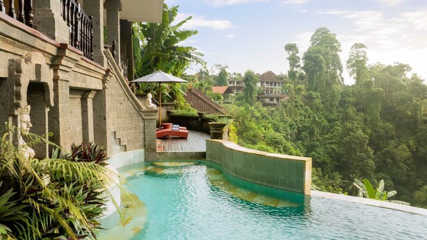 A curved infinity pool with a stone balustrade, a red lounge chair, and lush greenery surrounding the area. - 5 Bedroom Villa in Ubud with Jungle view (Ubud)