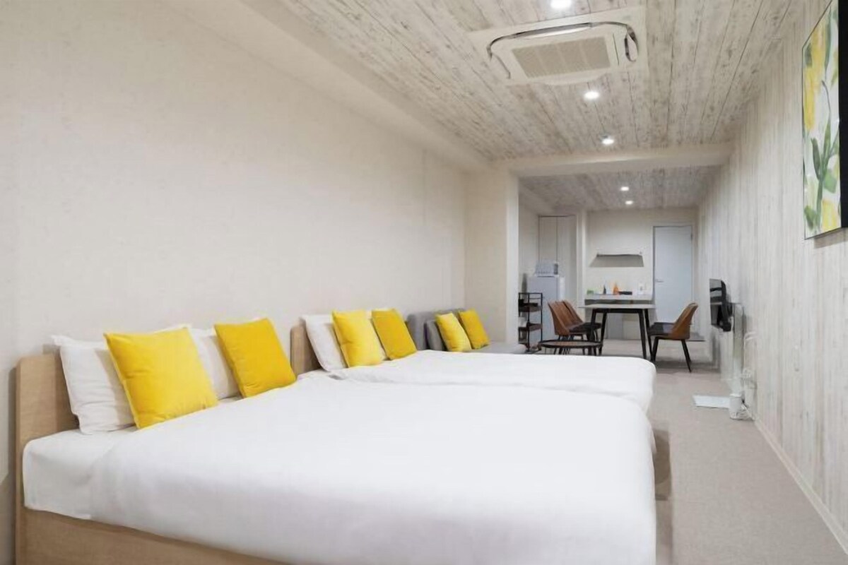 A hotel room with a large bed, a desk, and chairs, and a view into the dining area.