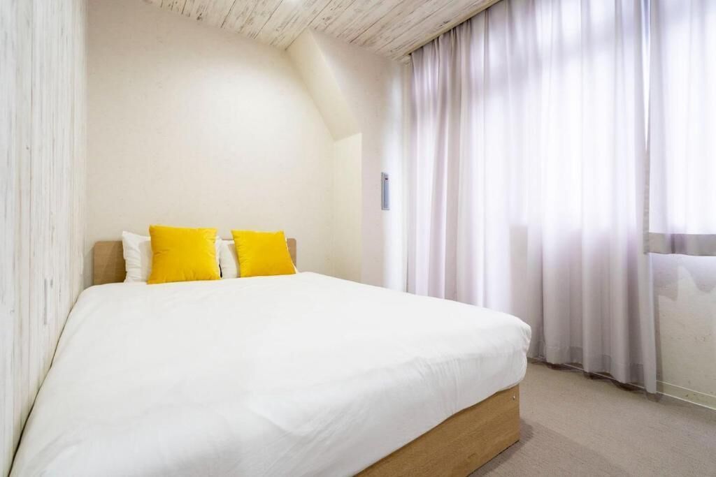 Una habitación con cama, paredes blancas y una ventana con cortinas.
