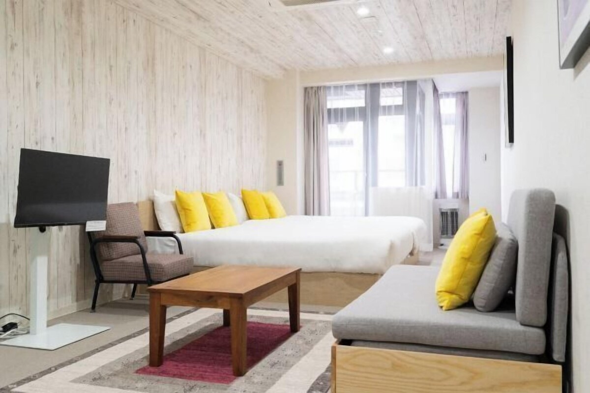 A modern hotel room with a bed, a sofa, a TV, and a desk.
