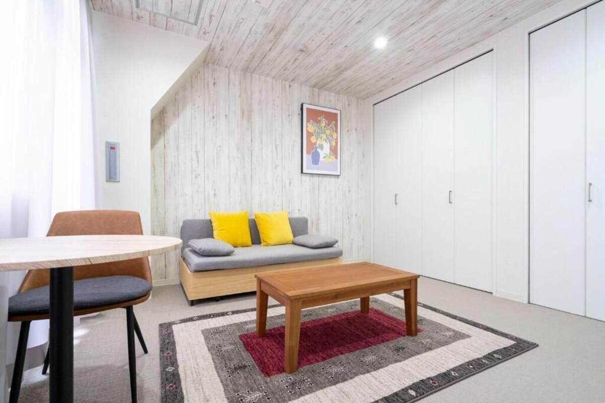 A modern living room with a wooden ceiling, a grey sofa with yellow cushions, a wooden coffee table, and a red rug.