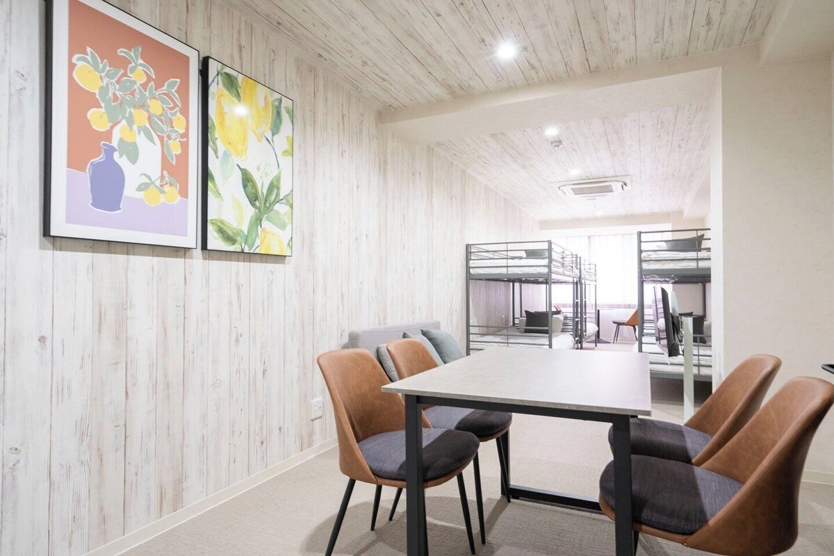 A conference room with a long table, four chairs, bunk beds in the background, and two framed artworks on the wall.