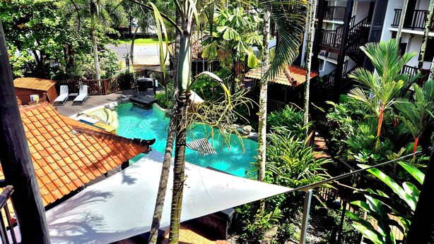 Une piscine entourée d’une végétation luxuriante et un bâtiment doté d’un toit en tuiles.
