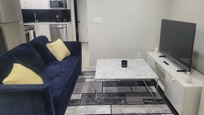 A compact living space with a sofa, a coffee table, a TV, and a kitchenette. - Elegant 2 Bedroom Suite - High-End Comfort! (Calgary)