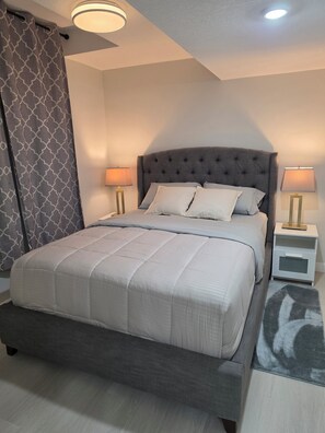 A neatly made bed with a tufted headboard, two bedside tables with lamps, and a patterned curtain.