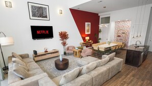 Ein modernes Wohnzimmer mit einer Eckcouch, einem Essbereich, einer Küche und einem an der Wand montierten Flachbildfernseher.