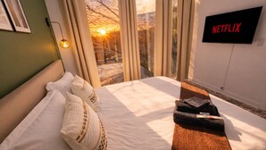 Ein Hotelzimmer mit Bett, Kissen, Fernseher und einem Fenster mit Vorhängen.