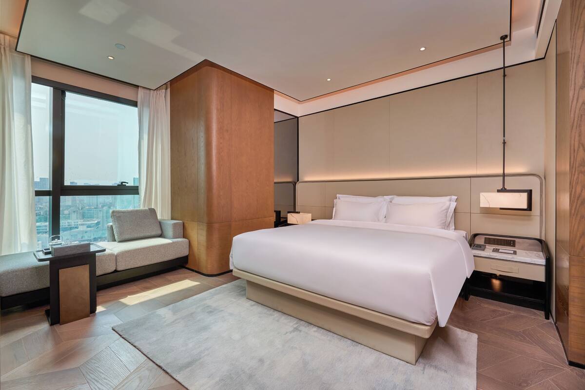 A modern hotel room with a large bed, a sofa, a small table, and a nightstand.