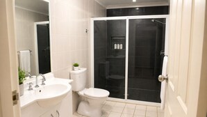 Un baño moderno con lavabo, inodoro y zona de ducha blancos.