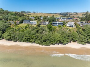 A coastal residential area with houses surrounded by dense greenery and a sandy beach.
