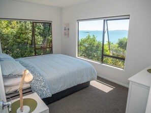 A bedroom with a bed, a desk, and a window with a view of trees and water.