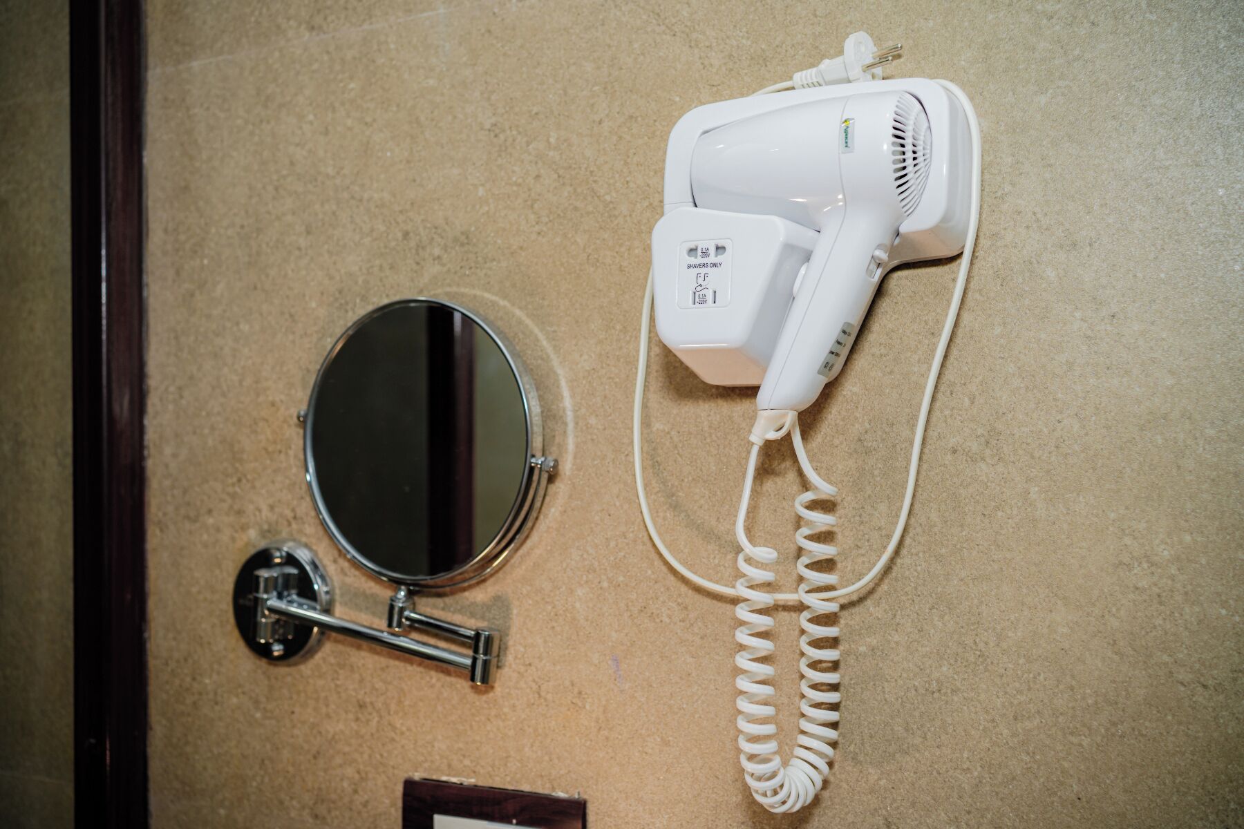 A hairdryer, a mirror, and a towel rack on a beige wall.