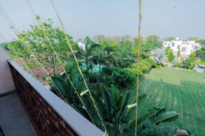 A balcony with a view of a well-maintained lawn, a swimming pool, and surrounding greenery.