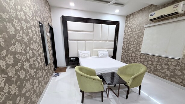 A hotel room with a bed, two chairs, a small table, and an air conditioning unit. - Hotel SR Executive Akola (Akola)