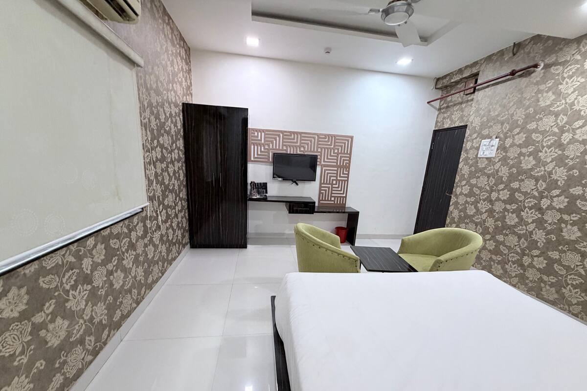 A hotel room with a bed, two chairs, a desk, a TV, and a wardrobe.