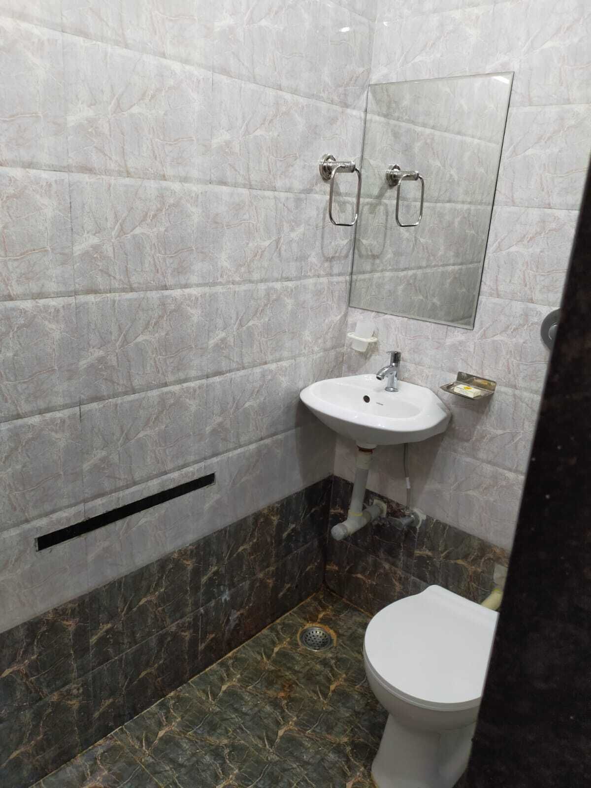A bathroom with a white sink, a toilet, a mirror, and marble flooring.
