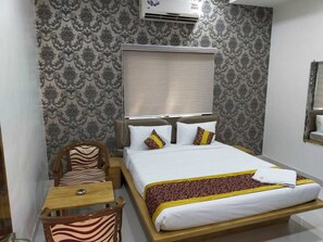 A hotel room with a bed, a wooden chair, a small table, and a window with blinds.