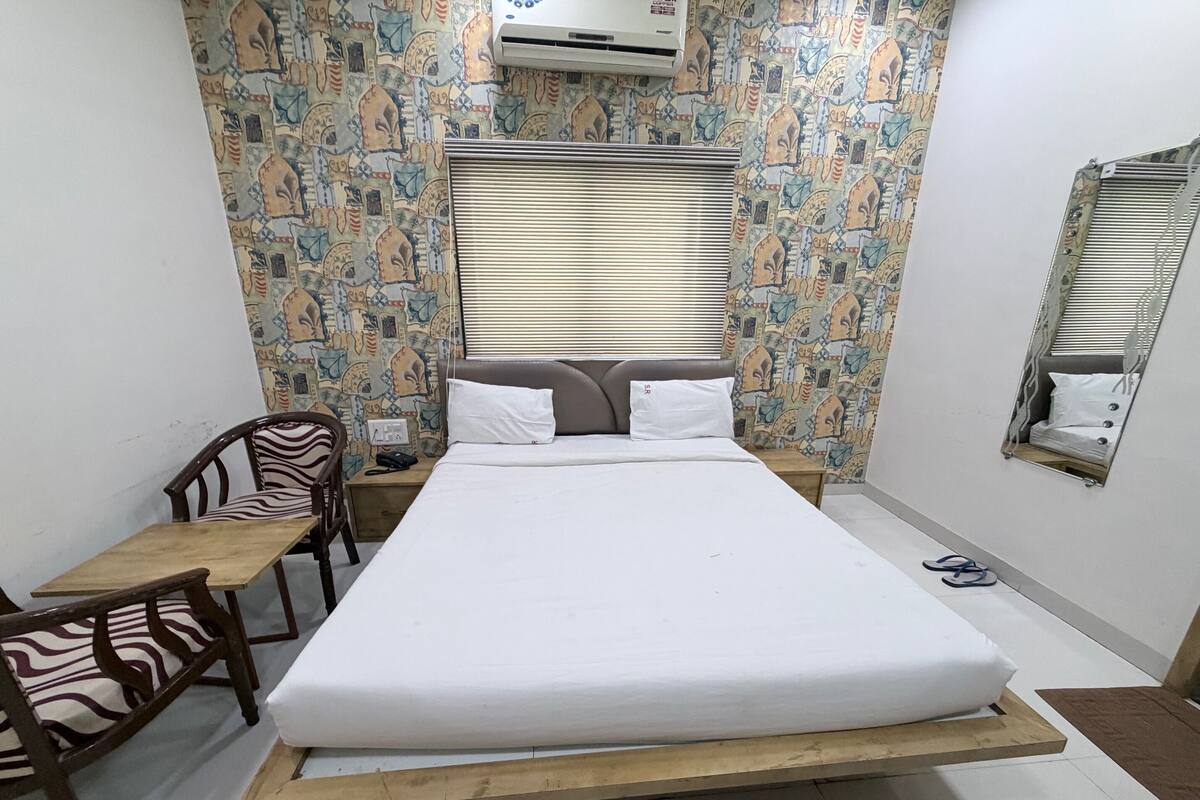 A bedroom with a bed, a desk, a chair, an air conditioner, and patterned wallpaper.